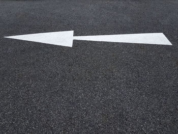 White traffic arrow symbol on asphalt road pointing to the left