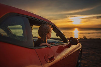 Girl looking though car window during sunset
