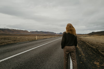 View from behind on woman standing on the road in iceland with her hair moving on the wind