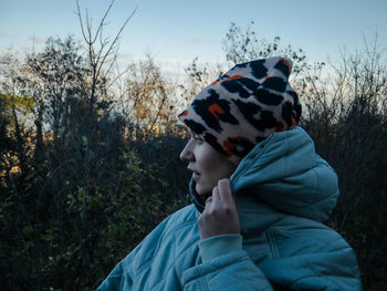 Smiling woman looking away while standing against trees during sunset