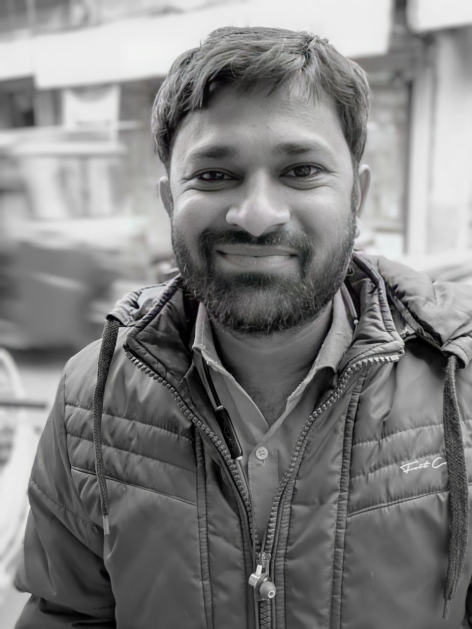 portrait, one person, men, black, adult, black and white, monochrome, looking at camera, beard, front view, smiling, facial hair, jacket, monochrome photography, person, architecture, city, happiness, clothing, headshot, focus on foreground, emotion, white, young adult, lifestyles, day, casual clothing, standing, human hair, city life, hairstyle, human face, outdoors, cheerful, leisure activity, street, waist up, building exterior