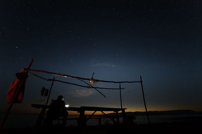 Silhouette people sitting on bench by the sea against sky at night