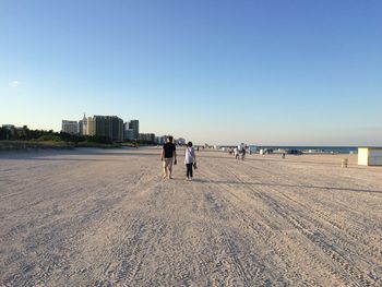 Low angle view of people walking at beach against clear blue sky