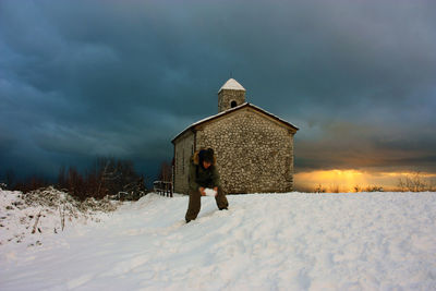 House on snow covered field by building against sky