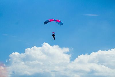 Low angle view of silhouette person paragliding against blue sky