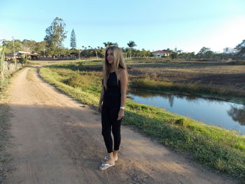 Full length of mature woman with long hair standing on dirt road against clear sky