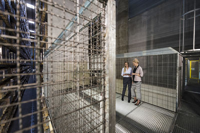 Women using laptop in high rack warehouse