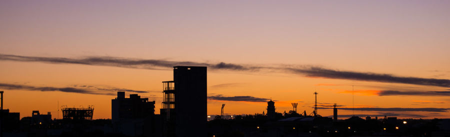Silhouette factory against sky during sunset