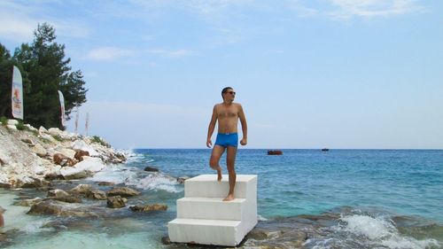Full length of shirtless man standing on steps in sea against sky