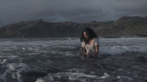 Woman sitting in sea against sky