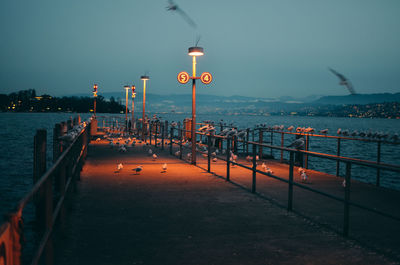 Illuminated pier over sea against sky at dusk