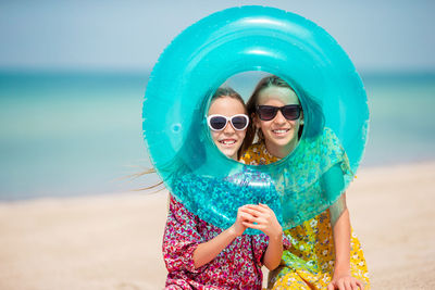 Portrait of sisters holding inflatable ring while standing at beach