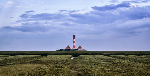 Lighthouse on field by building against sky