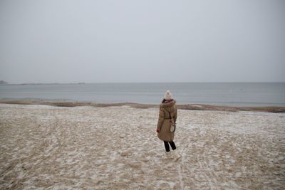 Rear view of woman walking on beach against clear sky