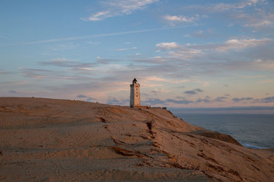 Lighthouse by sea against sky during sunset