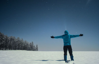Rear view of person standing on snow covered field against sky at night