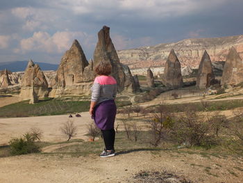 Rear view of woman standing on rock against cloudy sky