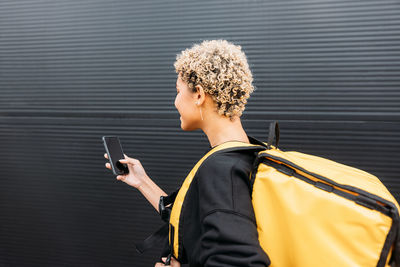 Side view of delivery person using mobile phone against wall