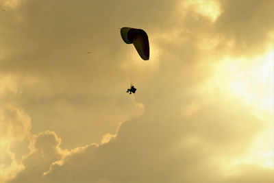 Low angle view of silhouette person paragliding against sky