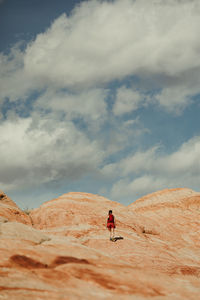 Woman hiker walks up a red rock hill towards blue cloudy skies in utah