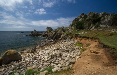 Rocks on shore by sea against sky