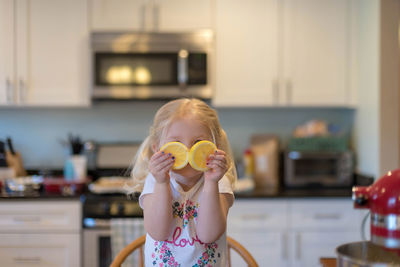 Cute girl holding lemon over face at home