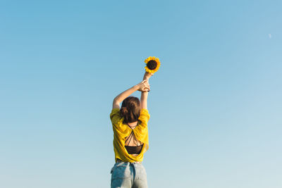 Low angle view of woman holding sunflower against sky