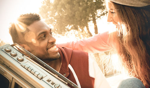 Close-up of cheerful young couple with radio against trees during sunset