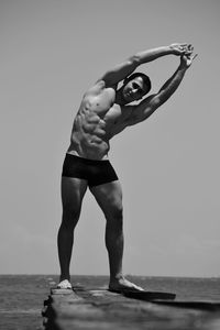 Full length portrait of bodybuilder exercising on pier over sea against clear sky