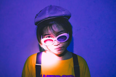 Portrait of young woman wearing sunglasses against blue wall