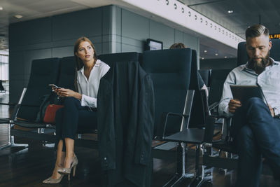 Thoughtful young businesswoman looking away while sitting with colleague in airport departure area