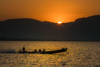 Silhouette boats in sea against orange sky