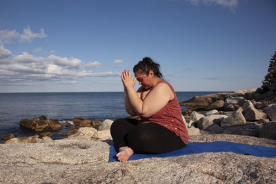 Woman sitting on rock at beach against sky