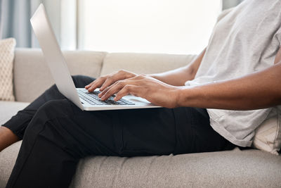 Midsection of woman using laptop while sitting on sofa at home