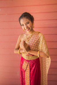 A young woman dressed in a yellow thai dress and raising her hand to say hello.