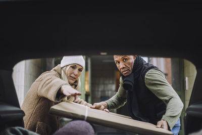 Mature woman guiding man loading cardboard in car trunk