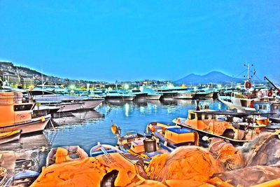 Boats moored at harbor against clear blue sky