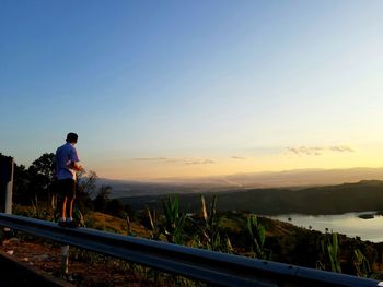 Side view of man standing on mountain against sky at sunset