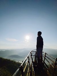 Rear view of man standing on railing against sky