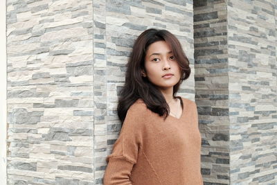 Portrait of beautiful young woman standing against wall