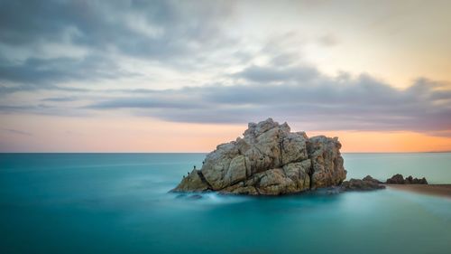 Rock formation in sea against sky during sunset