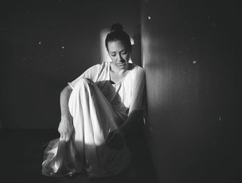 Young woman sitting in darkroom against wall