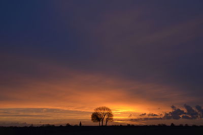 Silhouette trees on field against romantic sky at sunset