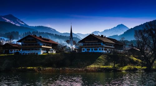 Houses by lake and buildings against sky