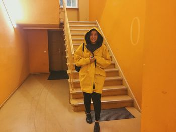 Full length portrait of woman wearing yellow raincoat by steps at home