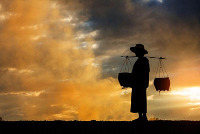 Silhouette man with containers standing against cloudy sky during sunset