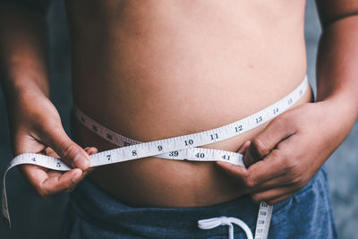 Midsection of shirtless boy measuring stomach