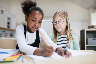 Girl assisting friend while studying in classroom at school