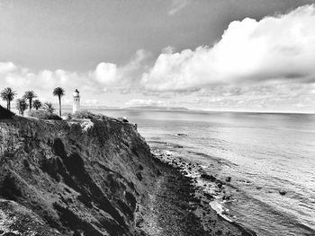 Cliff at beach against cloudy sky