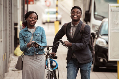 Portrait of smiling man and woman with bicycle on footpath